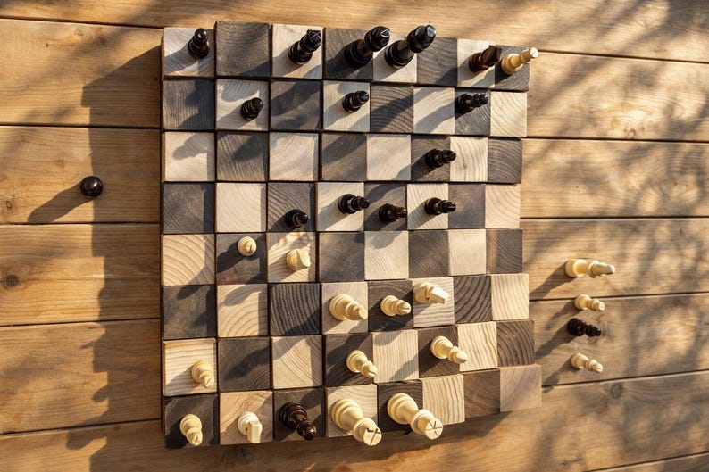 Puede incluir: Un juego de ajedrez de madera con un dise&ntilde;o &uacute;nico. El tablero de ajedrez est&aacute; hecho de cuadrados de madera claros y oscuros alternados. Las piezas de ajedrez son de color negro y crema. El juego se exhibe sobre una superficie de madera.