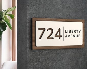 Puede incluir: Un letrero de número de casa de madera con fondo blanco. El número 724 está cortado en la madera y el texto "LIBERTY AVENUE" está impreso en negro debajo del número.