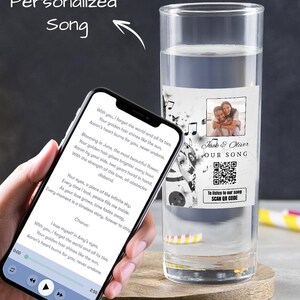 Puede incluir: Un vaso personalizado con un diseño en blanco y negro que presenta notas musicales y un código QR. El vaso tiene una etiqueta con el texto "Jack & Oliver Our Song" e instrucciones para escanear el código QR para escuchar la canción. El vaso está lleno de agua.