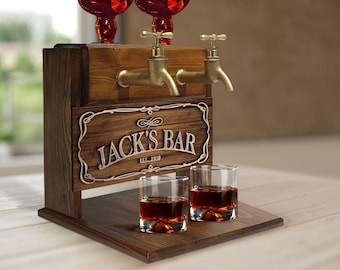 May include: Wooden bar cart with two liquor dispensers and a sign that reads "Jack's Bar Est. 2019". Two glasses of amber liquid are on the lower shelf.