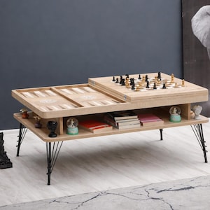 May include: A light wood coffee table with a backgammon board and a chess board. The table has black metal legs and a lower shelf with books and decorative items. A black and white elephant art print is in the background.