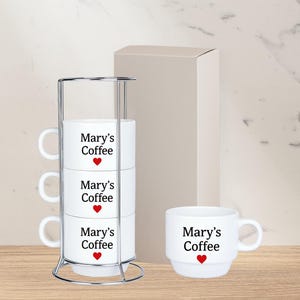 May include: Set of four white ceramic mugs with a red heart and the text "Mary's Coffee" on each mug. The mugs are stacked in a chrome stand.