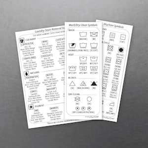 May include: Three white cards with laundry care instructions. One card details stain removal for various substances like coffee, wine, and blood. Another card shows wash and dry clean symbols. The third card displays iron symbols.