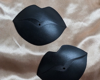 May include: Two black, 3D printed, lip-shaped ornaments with a small hole in the center of each.