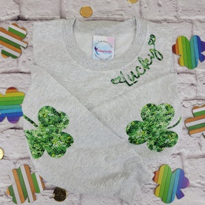 May include: A gray sweatshirt with the word "lucky" in green sequins on the front. The sweatshirt has two green sequin shamrocks on the sleeves.
