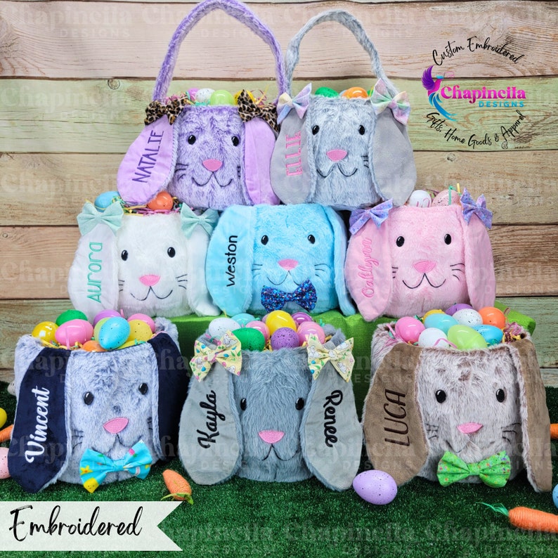 Puede incluir: Una colecci&oacute;n de cestas de Pascua de conejito de peluche en varios colores, incluyendo morado, gris, blanco, azul y rosa. Cada cesta est&aacute; bordada con un nombre y llena de coloridos huevos de Pascua. Las cestas tienen orejas ca&iacute;das y lazos.