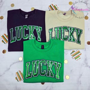 May include: Three sweatshirts in black, beige, and green with the word "LUCKY" in green sequins on the front.