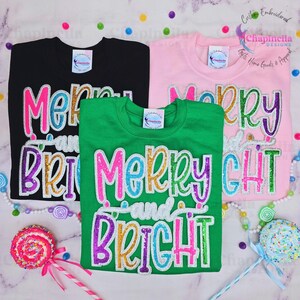 May include: Three t-shirts with the text "Merry and Bright" in colorful glitter letters. The shirts are black, pink, and green.