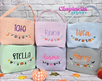 Pode incluir: Seis sacolas de tecido com padrões listrados em laranja, rosa claro, azul claro, verde claro, lavanda e preto. Cada bolsa apresenta nomes bordados, incluindo Tate, Reina, Luca, Stella, Aurora e Henry, com guirlandas temáticas de Halloween.