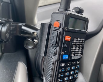 以下が含まれることがあります： デジタルディスプレイとキーパッドを備えた黒い双方向無線機。無線機は黒いブラケットを使用して車に搭載されています。無線機には、「PTT」、「MON」、「CALL」、「VFO/MR」、「A/B」、「MENU」、「STEP」、「VOX」、「TOR」、「UV-5R  MKS P」というラベルの付いたボタンがあります。