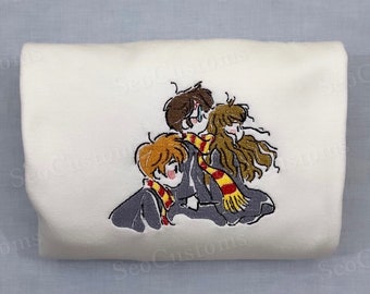 May include: White embroidered sweatshirt featuring a cartoon illustration of three friends from the Harry Potter series. The friends are wearing Hogwarts school uniforms and scarves.