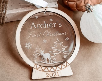May include: A wooden Christmas ornament with a clear acrylic insert featuring a deer and trees. The ornament is engraved with the text "Archer's First Christmas 2021".
