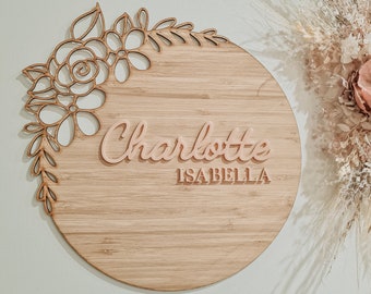 Może przedstawiać: Okrągły drewniany znak z kwiatowym wzorem i imionami "Charlotte Isabella" w różowych literach.