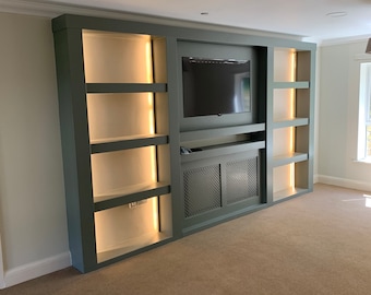 May include: A built-in entertainment unit with a dark green finish and a flat screen TV. The unit has shelves with warm white LED lights and a lower cabinet with a metal grille.