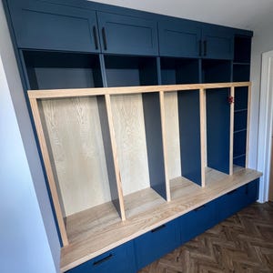 May include: A bespoke navy blue storage unit with multiple compartments. It features upper cabinets with black handles, open cubbies, and lower drawers. The unit has a light wood bench and frame.
