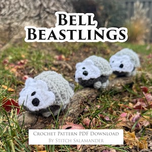 May include: Three crocheted creatures with grey bodies and white faces are displayed outdoors. The text "BELL BEASTLINGS" is at the top of the image. Below the creatures is a white banner that reads "CROCHET PATTERN PDF DOWNLOAD BY STITCH SALAMANDER."
