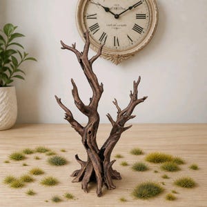 May include: A brown, textured, leafless tree sculpture with a gnarled, branching trunk and exposed roots, surrounded by numerous small, circular patches of green artificial grass tufts scattered across the surface around the base.
