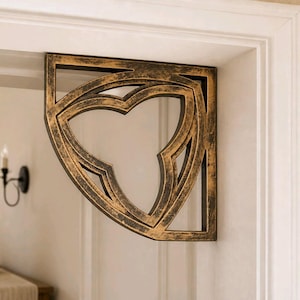 Könnte beinhalten: Verziertes, bronzefarbenes Zierkonsolen mit einem gotisch inspirierten Design. Die Konsole ist an einem weißen Türrahmen befestigt und weist ein stilisiertes, durchbrochenes Muster mit einer zentralen Kleeblattform auf. Die Oberfläche der Konsole hat ein gealtertes Aussehen.