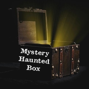 May include: An open, antique-style wooden box with the text "Mystery Haunted Box" in white. The box is brown with metal accents and a dark interior, illuminated by a golden light.