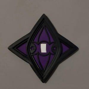 May include: A decorative light switch cover with a gothic design. The cover is black with a purple center and a white switch. The design includes star and arch details.