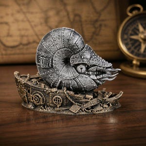 May include: A silver-toned, metallic-looking nautilus shell sculpture with mechanical, riveted panel details, resting atop a weathered, bronze-coloured ship wreck base featuring small portholes, chains, and debris textures.