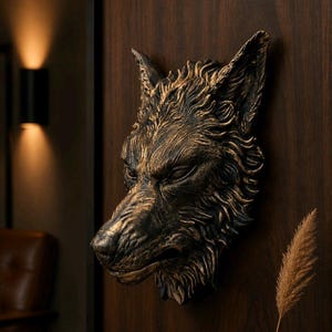 Op de afbeelding: Een bronzen wolfskopsculptuur gemonteerd op een donkerhouten paneel. De sculptuur heeft gedetailleerde vachttextuur en een strenge uitdrukking. De achtergrond bevat een wandlamp en een vleugje leren stoel.
