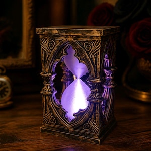 May include: A rectangular hourglass with a weathered bronze-coloured frame featuring intricate carved details. The central glass chamber contains glowing purple sand, illuminated from within, creating a vibrant contrast against the dark metallic structure.