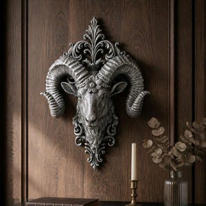 May include: A silver-colored ram head wall sculpture with large, curved horns and floral detailing. The sculpture is mounted on a dark wood panel. A candle and vase of dried flowers are in the foreground.