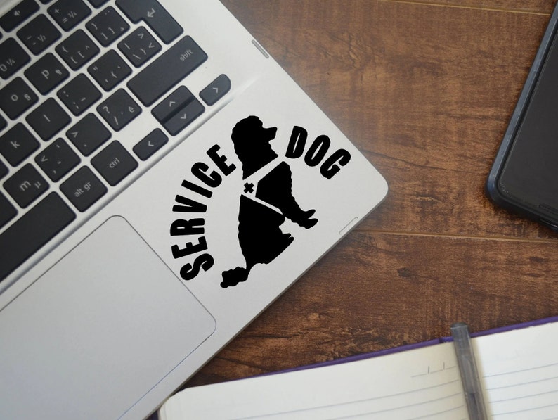 May include: A black and white sticker of a poodle with a service dog vest on a silver laptop. The sticker says "SERVICE DOG" in black text.