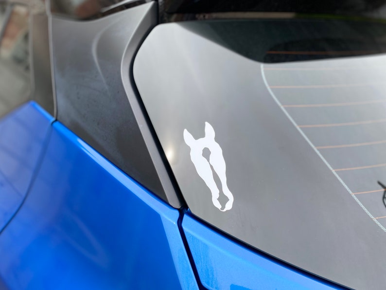 Puede incluir: Un coche azul con una pegatina de cabeza de caballo blanca en la ventana trasera.