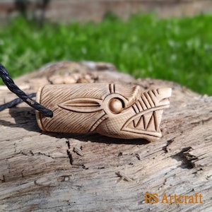 May include: A carved wooden pendant in the shape of a dragon's head. The pendant is light brown and has intricate details, including a large eye and sharp teeth. The pendant is attached to a black cord.