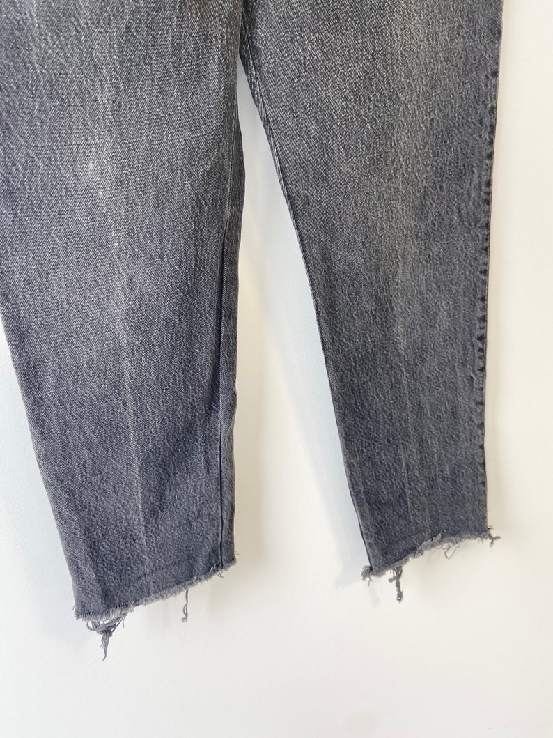 May include: A pair of dark gray denim jeans with a frayed hem.