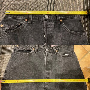 May include: A pair of black denim jeans with a yellow measuring tape across the waistband. The tape measures 38 inches.