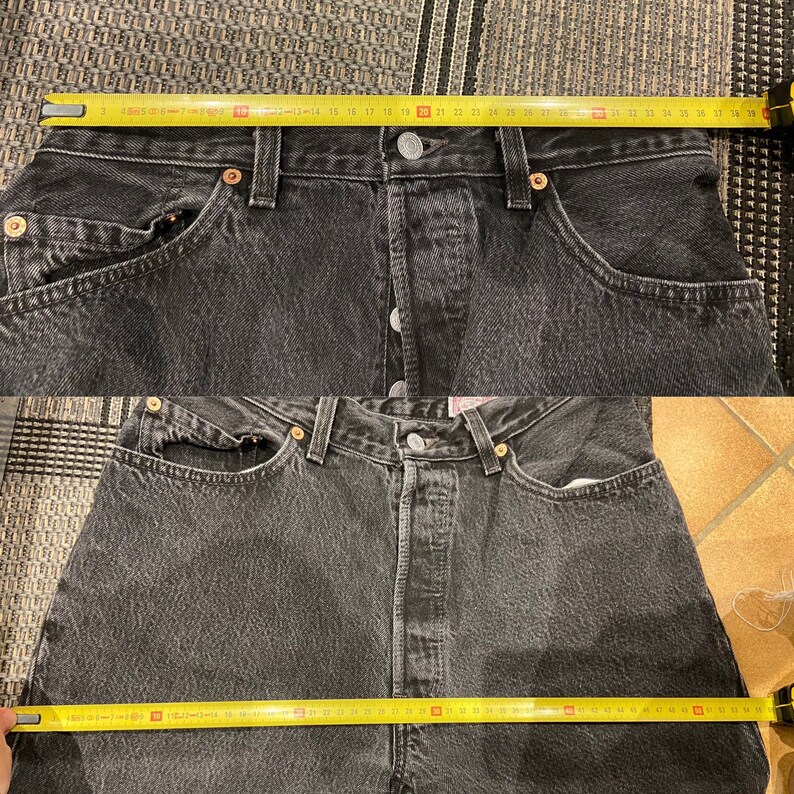 May include: A pair of black denim jeans with a yellow measuring tape across the waistband. The tape measures 38 inches.