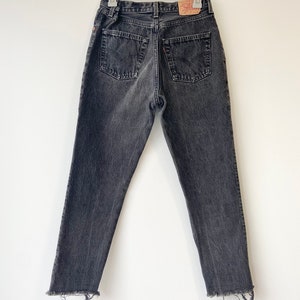 May include: Black denim jeans with a frayed hem. The jeans have a classic five-pocket style and a Levi's brand patch on the back.