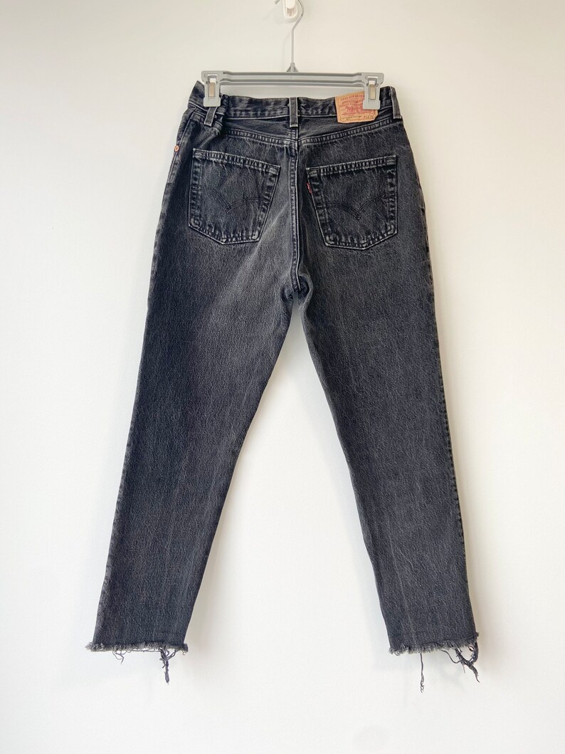May include: Black denim jeans with a frayed hem. The jeans have a classic five-pocket style and a Levi's brand patch on the back.