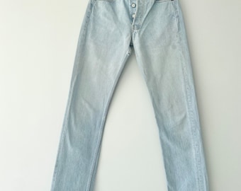 May include: Light blue denim jeans with a button fly and a straight leg. The jeans have a slight slit at the bottom of each leg.