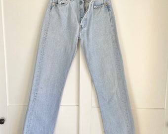 May include: Light blue denim jeans with a button fly and a straight leg. The jeans are hanging on a black hanger.