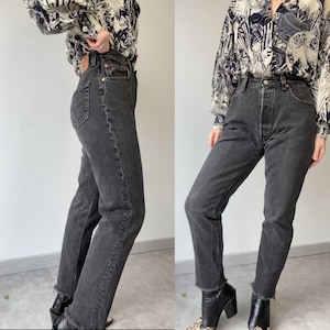 May include: A pair of black denim jeans with a high waist and a straight leg fit. The jeans have a frayed hem and are shown on a model wearing a patterned blouse.