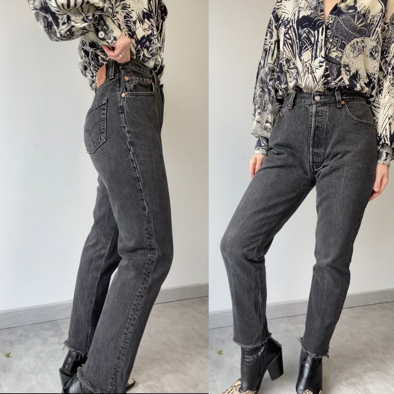 May include: A pair of black denim jeans with a high waist and a straight leg fit. The jeans have a frayed hem and are shown on a model wearing a patterned blouse.