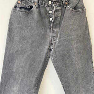 May include: A pair of dark gray denim jeans with a button fly and five pockets.