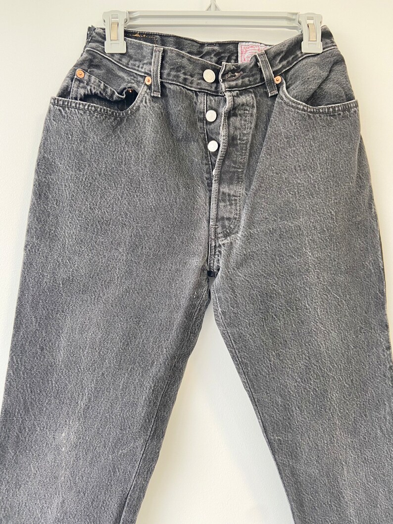 May include: A pair of dark gray denim jeans with a button fly and five pockets.