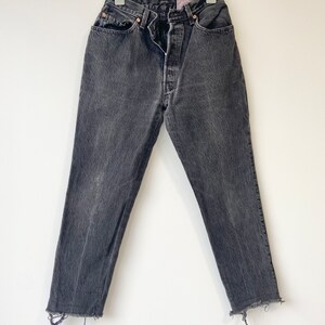 May include: Black denim jeans with a frayed hem. The jeans have a classic five-pocket style and a button fly.