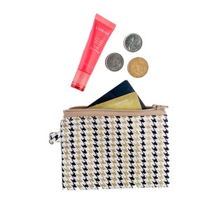 Peut inclure: Une pochette zippée à motif noir et blanc avec une carte de crédit dorée et des pièces à l'intérieur. La pochette est ouverte et un tube rose de masque de nuit pour les lèvres LANEIGE est posé sur la pochette.