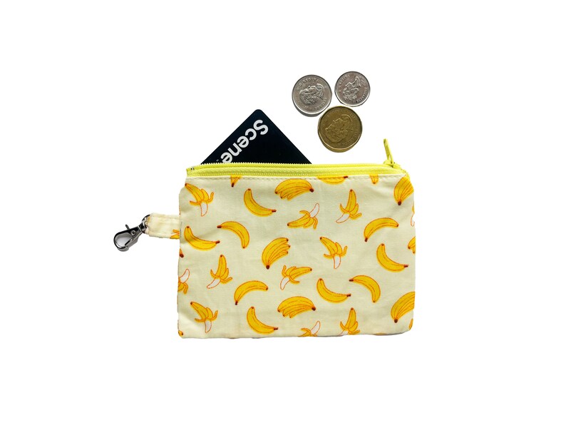 May include: A small yellow zippered pouch with a banana print. The pouch has a silver clip and a black card inside. Three silver coins are on top of the pouch.