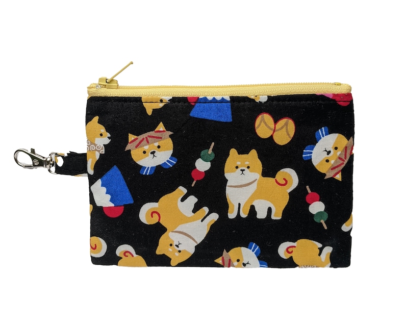May include: A black zippered pouch with a yellow zipper pull. The pouch is decorated with a repeating pattern of Shiba Inu dogs, Japanese food, and traditional Japanese clothing.
