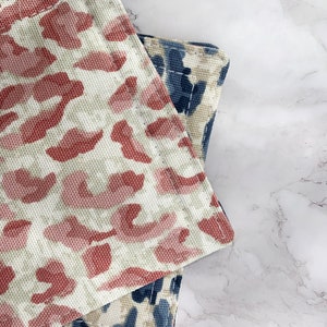 May include: Two fabric kitchen pot holders with a leopard print design. One is pink and white, the other is blue and white.