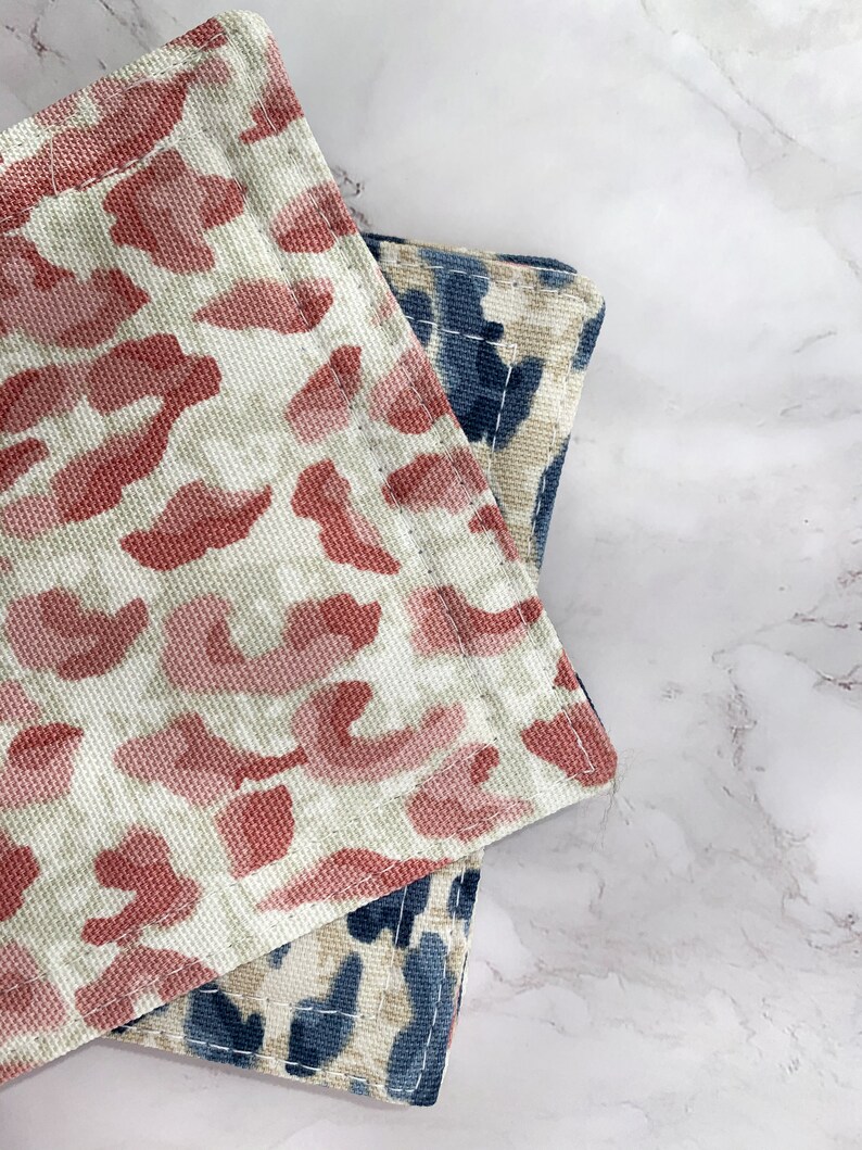 May include: Two fabric kitchen pot holders with a leopard print design. One is pink and white, the other is blue and white.