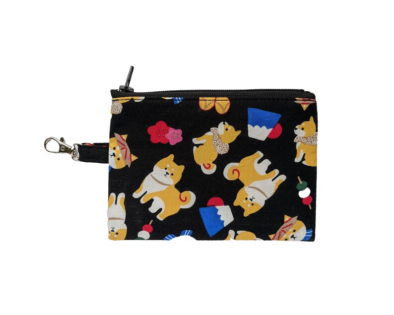 May include: Black zippered pouch with a repeating pattern of Shiba Inu dogs, Japanese sweets, and flowers. The pouch has a silver metal hook.