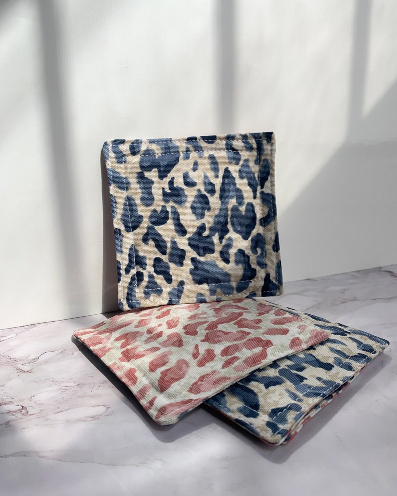May include: Three fabric coasters with a leopard print design. The coasters are in shades of blue, pink, and beige.